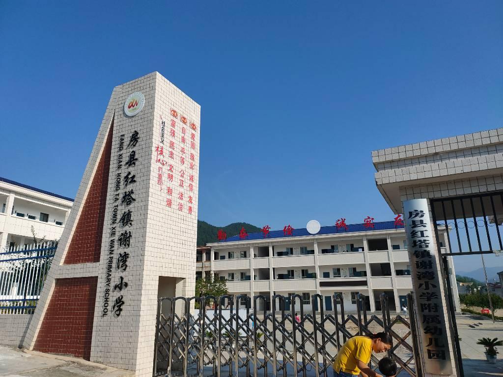 图为红塔镇谢湾小学校门，除了挂牌谢湾小学外，还挂牌了其附属幼儿园，从这儿可以看见“勤奋节约，诚实友善”的校训。校门正对着的这栋楼就是幼儿园至五年级的教学楼，二楼右侧是教师办公室。