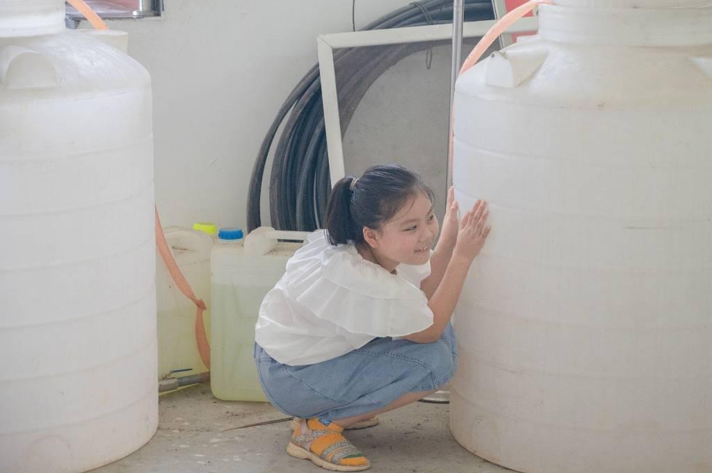 图为一位小朋友与伙伴们一起玩捉迷藏，小朋友偷偷躲在了一个大水桶的后面，满脸期待地观察着伙伴们，希望自己不会被发现。  安徽师范大学 刘昕 摄