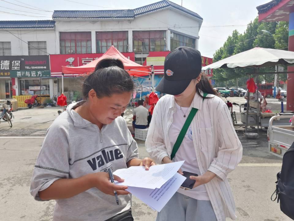 图为实践团成员在大年陈镇发放调查问卷，并帮助居民逐步完成调查问卷的填写。