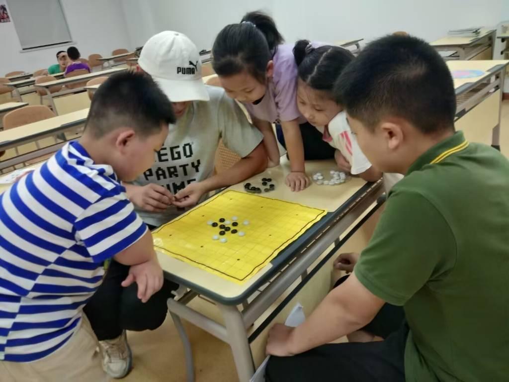 图为志愿者老师与学生进行五子棋博弈，其余学生前来助阵（大学生网报通讯员 刘菊芳摄）