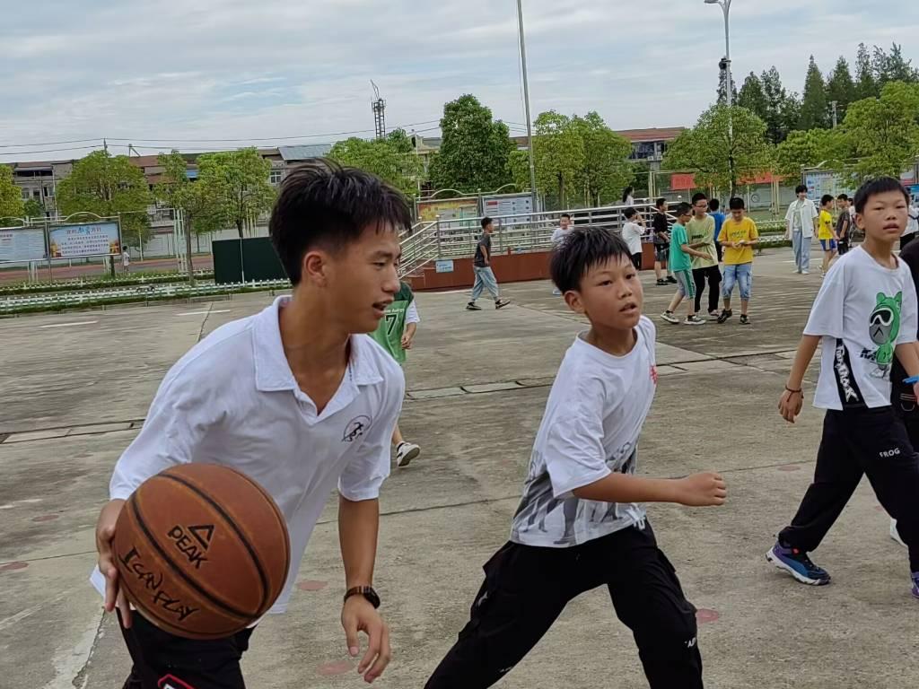 图为课下实践队员陪同学生进行篮球练习，用体育带给学生快乐，让学生在体育运动的陪同下健康成长。