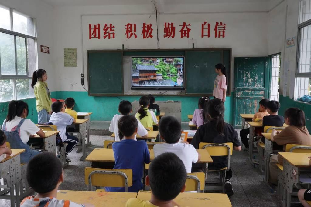 图为支教队员为学生讲解民族文化的基本知识，在讲解到土家族的基本住宅时，同学们都听得很认真并且积极地在进行互动。通讯员田柯锐