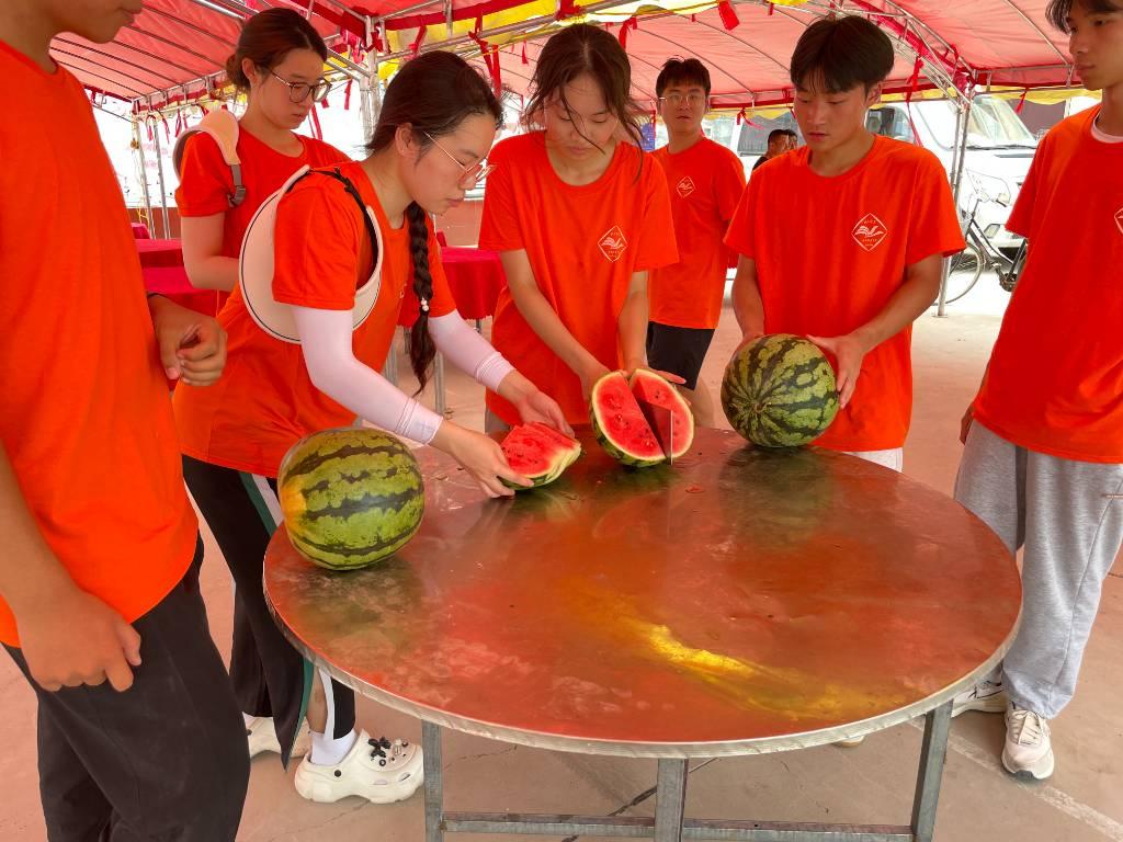 ﻿﻿图为助梦团成员一起为孩子们切好由当地居民热情送来的西瓜。中国青年网通讯员 李静怡 供图