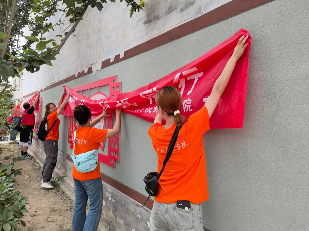 图为实践队员们在龚楼村墙面上挂“新时代理论”宣讲条幅。大学生网报通讯员 付子文 摄