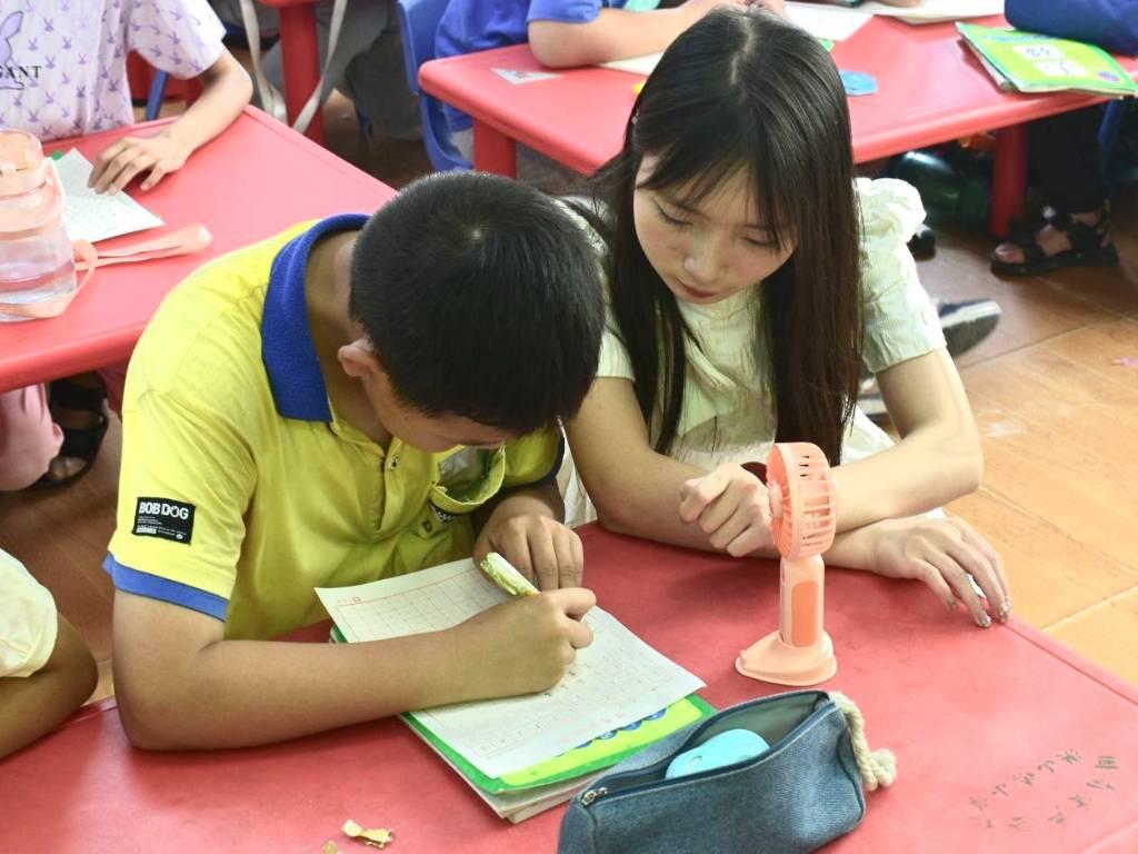 图为志愿者在书法课上细心为小朋友讲解书法要领并指出其书法重存在的问题。中国青年网通讯员 景思溢 摄