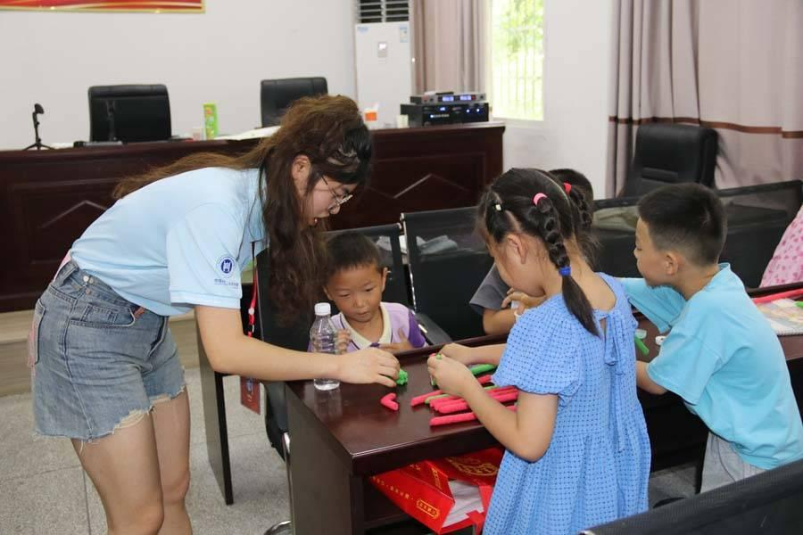 华中师范大学物理科学与技术学院党员国情学习与实践队队员在协助孩子做环保棒手工