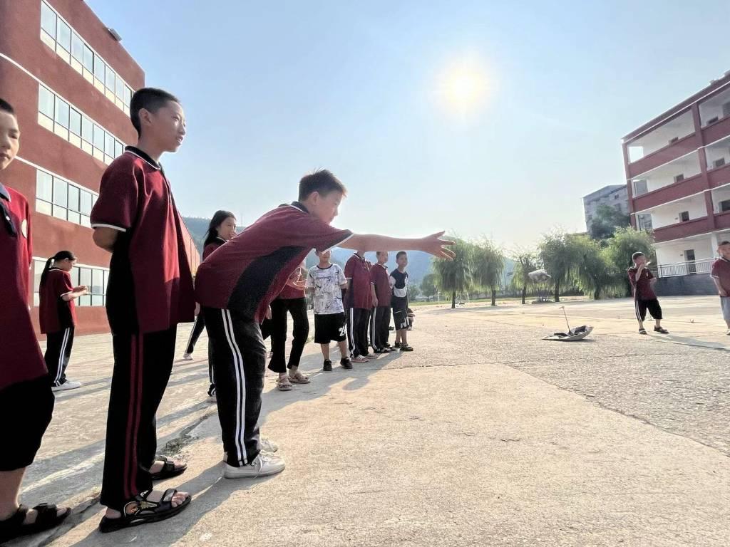 图为趣味运动项目的投沙包活动，图中的少年正弯腰，试图将沙包投向正中的红心上。