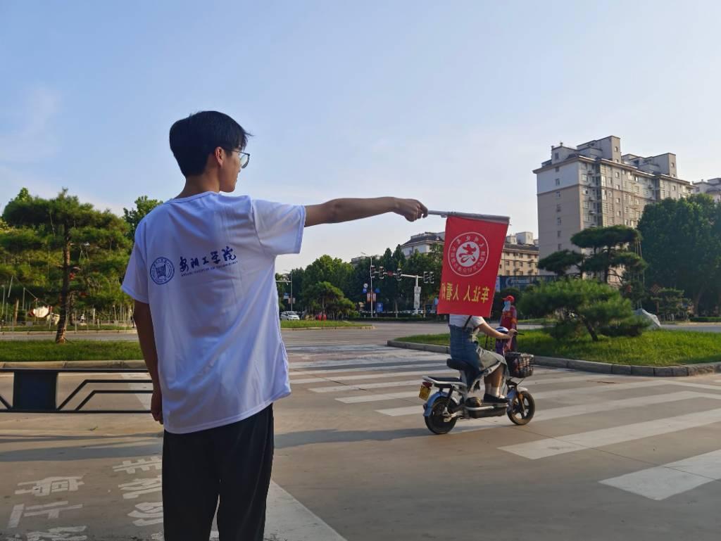 图为社会实践成员在路边维护交通秩序。 刘伟平表示，在路边做志愿者的时候，自己主要负责的是检查电动车车驾驶人及乘车人在通行道路时，是否规范戴安全头盔。他说:“大部分人都是有佩戴头盔的，但有一小部分人还是没有佩戴头盔，头盔在必要的时候是可以保护我们生命安全的，希望广大市民，自觉遵守交通法律法规，共同营造安全文明的道路交通环境。 中国青年网通讯员 刘伟平 供图