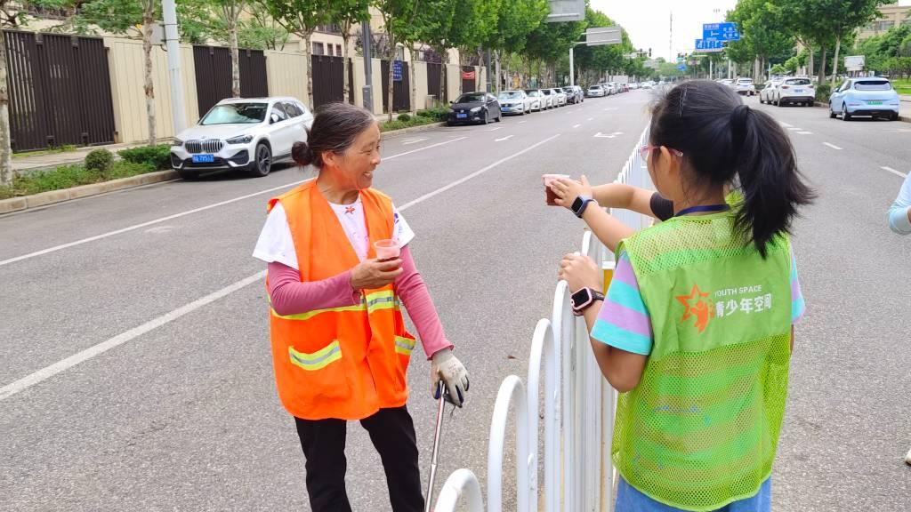 图为小朋友们双手拿着酸梅汤给路边打扫卫生的阿姨送清凉，阿姨表示感激。中国大学生网报通讯员 赵梓茗 摄