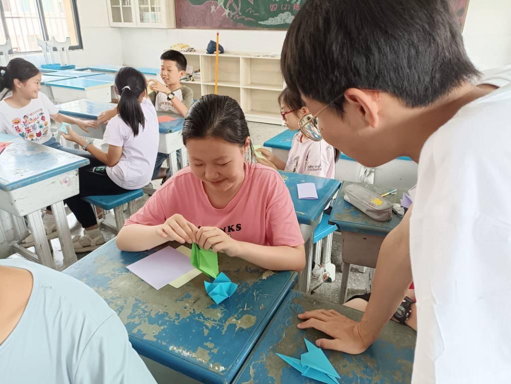 折纸，最初是来自于中国，通过丝绸之路传播到世界各地。它既是一种艺术形式，也可以变成实用的物品。通过折纸，孩子们可以学习到几何、数学、物理等知识。当他们在折叠的过程中探索形状、角度和纹理时，他们也在培养空间想象力和逻辑思维能力。为让孩子们充分感受折纸的艺术魅力和探索其中几何和物理的乐趣，湖北汽车工业学院科技学院青锋·文源志愿服务队于7月18日在南漳县巡检完全小学给孩子们上了一节折纸课。