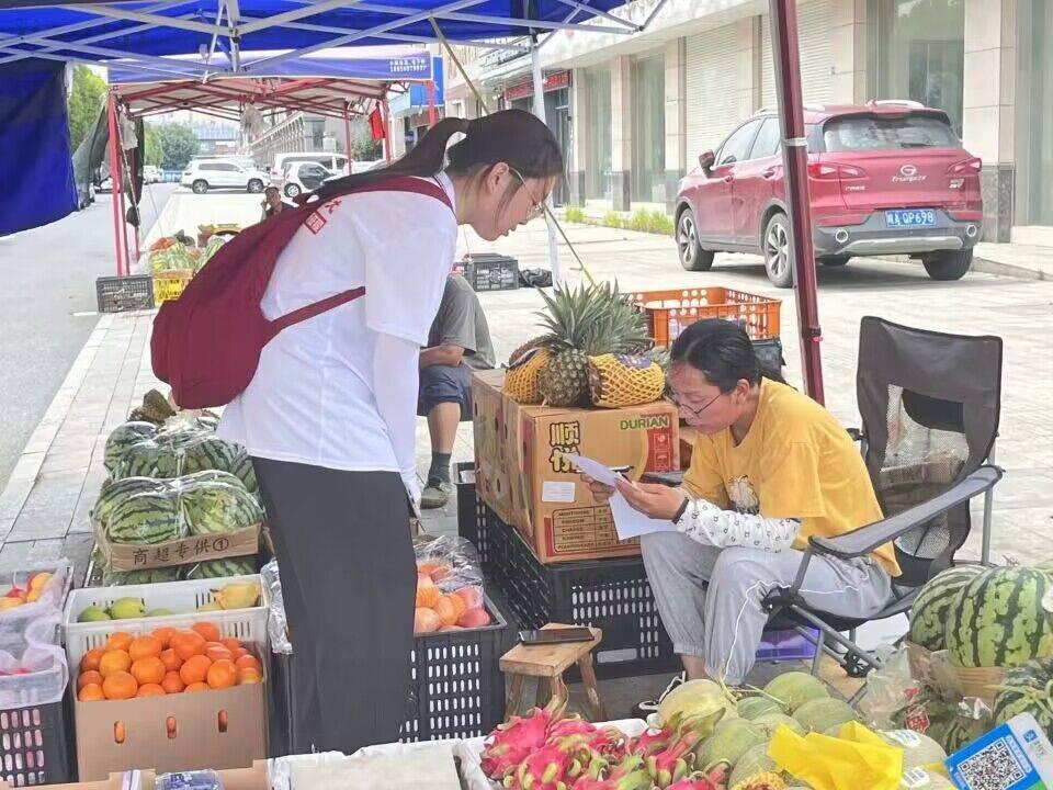 图为实践队员走进集市对贩卖水果的阿姨进行有关献血的问卷调查和宣传，实践队员和阿姨聊起献血经历。