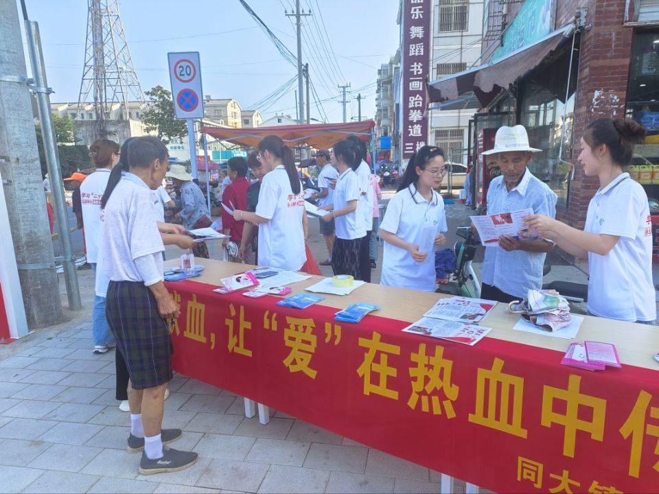 图为实践队员在人流量大的集市拉横幅进行有关无偿献血的宣传活动，为来往人员讲解有关献血的知识。