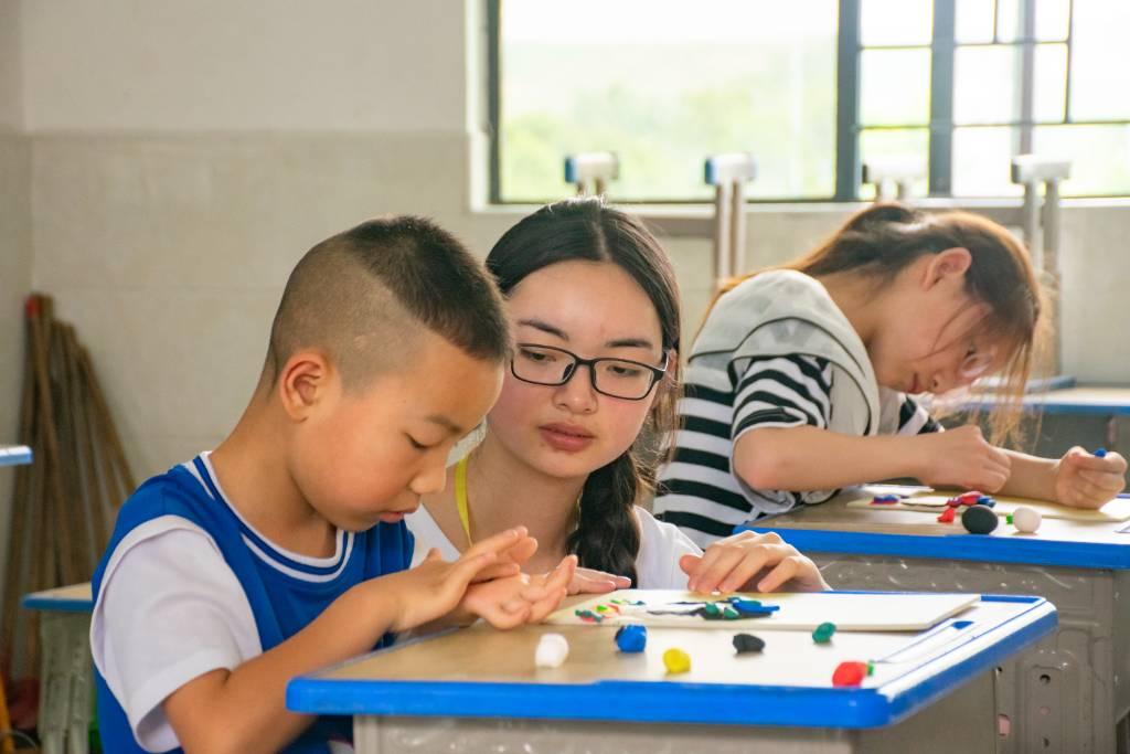 队员耐心指导学生制作粘土作品，队员给学生讲解超轻粘土的使用方法，并提供各种图案供学生选择，让每个人都能制作出心仪的作品