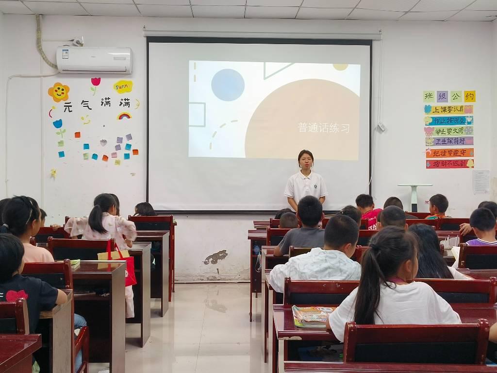 图为团队成员教学生普通话课。学好普通话可以提高我们的语言表达能力。普通话是形式最规范、最标准的语言，因此学会使用普通话可以锻炼我们的口语表达能力和思维能力，让我们的表达更加准确、清晰。