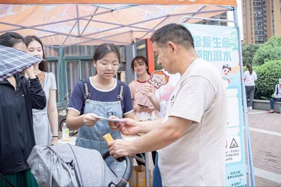 图为队员在给社区居民宣传防溺水知识，分发防溺水知识手册。 中国大学生网报通讯员 刘鸿旺 提供