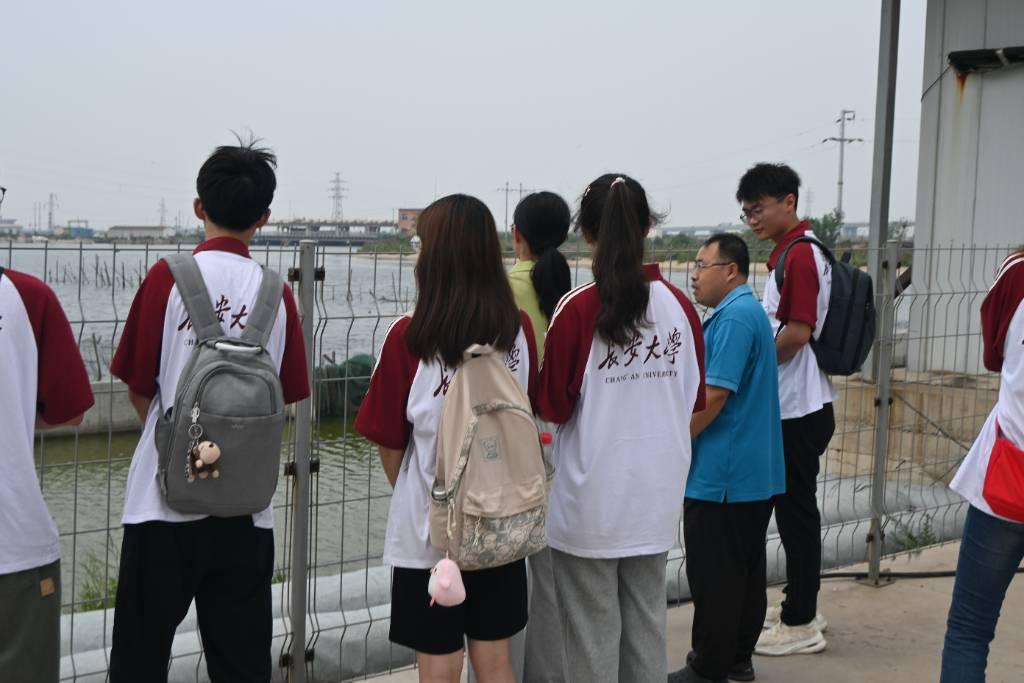 图为工程师带领实践队成员参观水产养殖车间外景，帮助同学们进一步了解该企业的具体运营状况以及水产养殖情况。