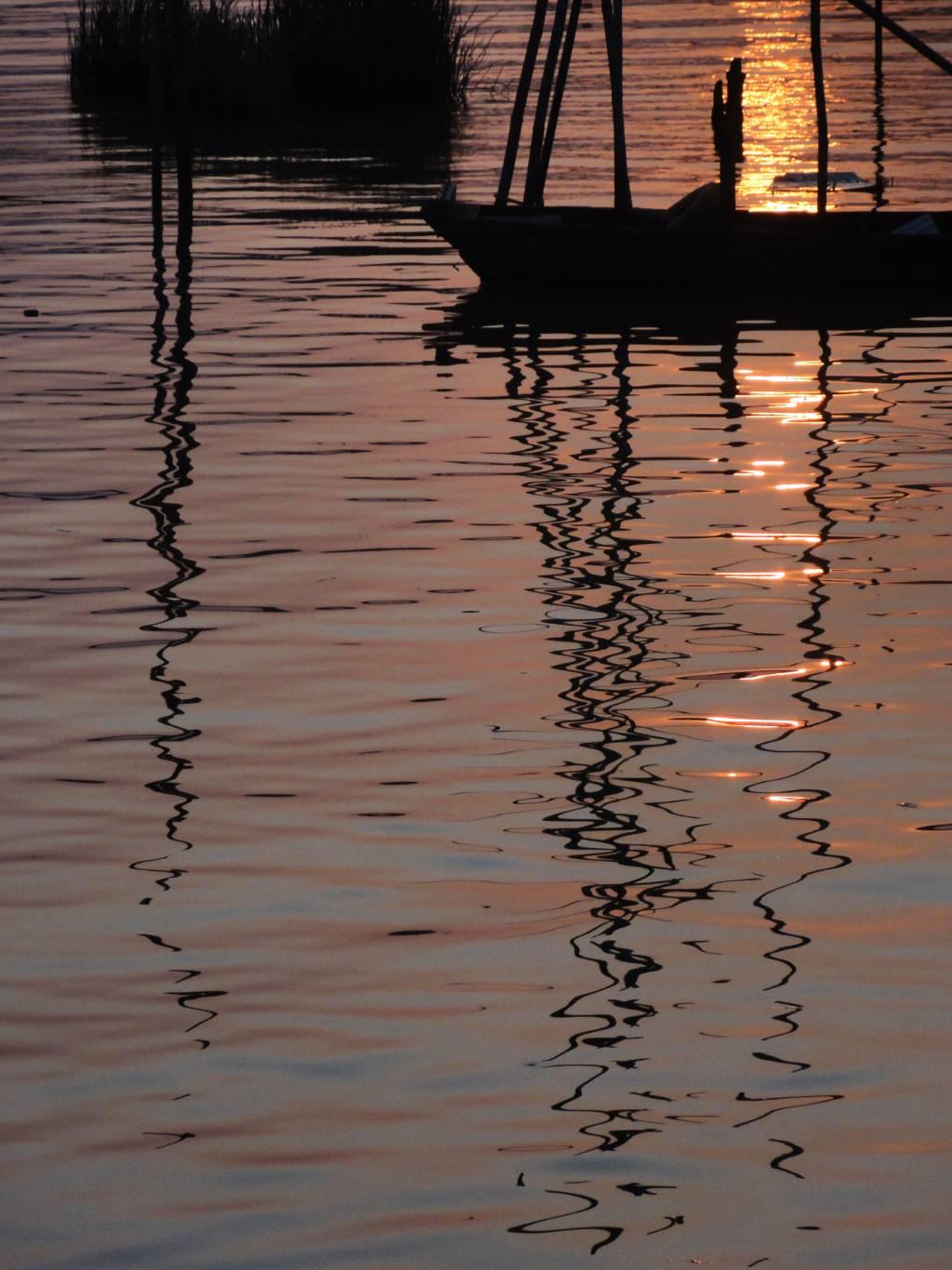 船只在水面上静静停泊，夕阳倒影映照其旁，犹如画中美景，船影与夕阳交相辉映。