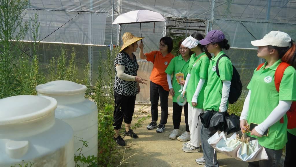 2023.7.10 火龙果种植园的奶奶正在和实践队队员们介绍酵素的制作。用洗净的厨余垃圾和水放入照片中的白色大桶中发酵制作酵素，可用于火龙果的施肥，达到绿色低碳健康的效果。