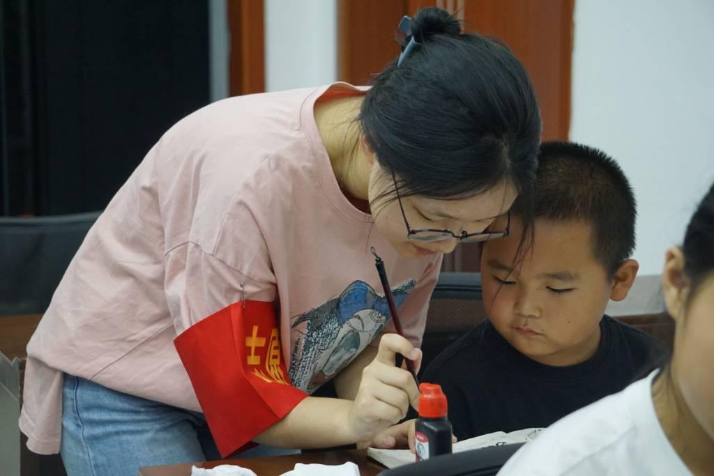 小朋友在志愿者的指导下，学习如何使用毛笔写出漂亮的中国字