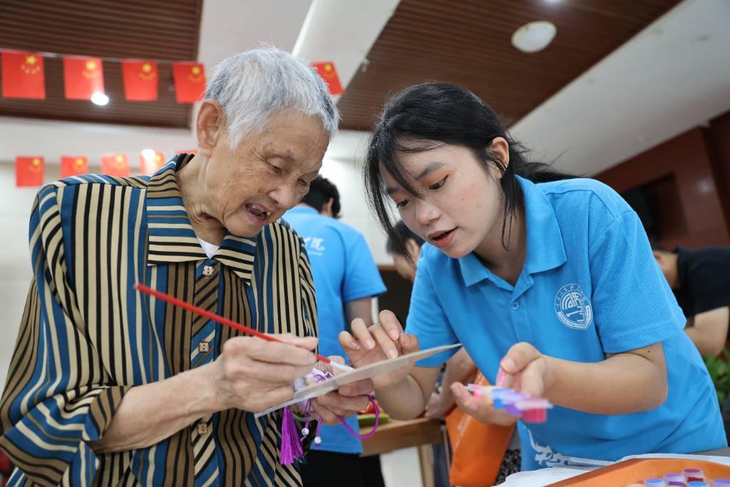 实践团成员和老人共同绘制扇子 特约摄影 赵勇