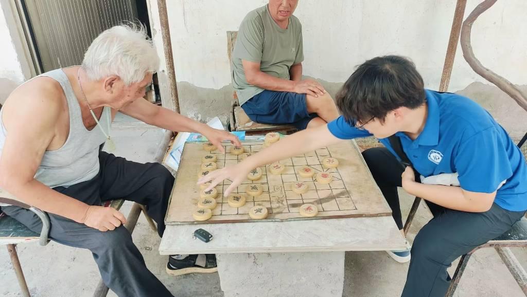 图为实践团成员与村中老人下象棋