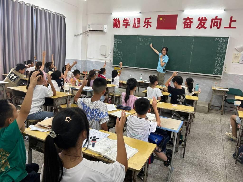 图为四年级学生在实践队成员韦理莹的引导下，积极举手、参与模拟人生的小游戏。实践队成员李亚男。