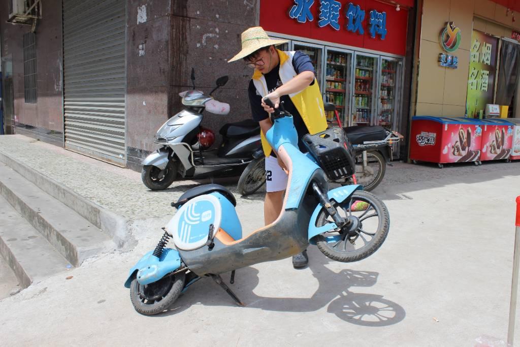 图为志愿者扶起路边倒地的共享电动车。通讯员 何梓聪 摄